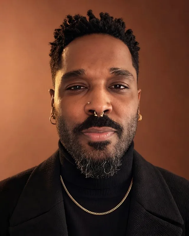 Portrait of Anthony Arlene with a slight smile, wearing a gold chain over a black turtleneck.